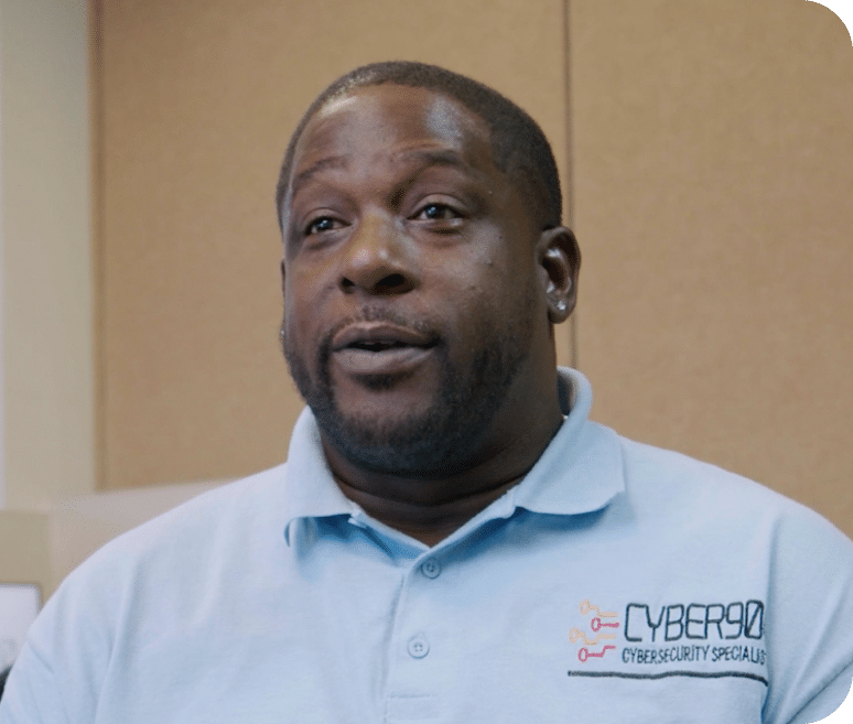 A person in a light blue polo shirt with the Cyber90 Cybersecurity Specialists logo is speaking. The beige walls create a neutral background, perfect for maintaining focus. This setting is ideal for Video Section2, emphasizing key SEO keywords without distractions.