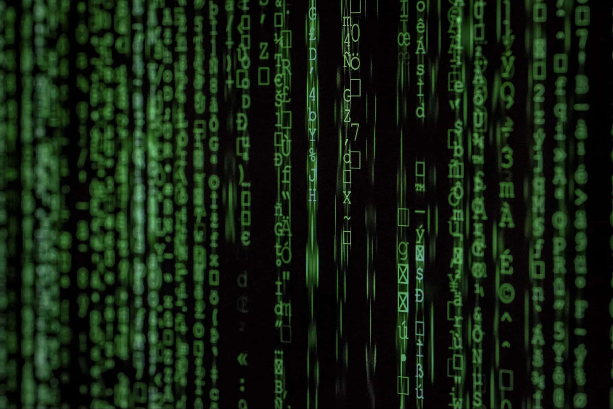 Green digital code streams down a black screen, resembling the iconic Matrix movie effect, with various symbols, letters, and numbers appearing in vertical columns—evoking the intricate workflows of MSPs managing cybersecurity in a multi-tenant model.